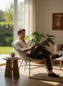 Paniery Signature Atlas Chair, handwoven from recycled fishing lines in a light grey, with a sculptural open design, shown with a man reading.