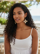 Paniery handcrafted earrings featuring cream cowrie shells arranged in a clover shape with gold-tone wire accents.