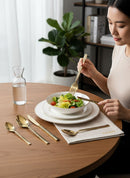 Paniery gold cutlery set with Adinkra wave and crossed patterns, a woman dines.