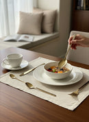 Paniery gold cutlery set with Adinkra symbols, including spoons and a fork, on a table setting.