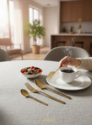 Paniery gold cutlery set with Adinkra design, featuring forks and spoons, displayed on a table with a bowl of cereal and a cup of coffee.