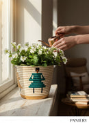 Paniery handwoven basket with bold teal graphic pattern, natural straw base, holding white flowers. Used for decor or storage.