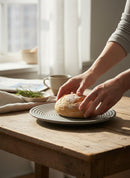 Paniery grey ceramic plate with concentric circle design, holding a bread roll.