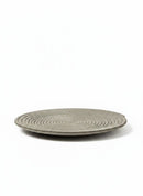 Paniery handwoven grey sisal and raffia flat plate with concentric circle texture and asymmetrical edge detail.