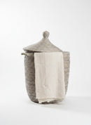Paniery handwoven grey laundry basket made from recycled plastic and natural fibers with leather handles. Features a lid and a cream cloth.