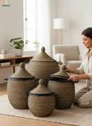 Paniery luxury handwoven laundry basket in natural fibers with black leather trim, available in multiple sizes. A woman is shown placing the lid on one basket.