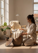 Paniery luxury handwoven laundry basket in Senegal, natural fibers with full leather trim, includes lid. Woman arranging blankets.