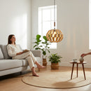 Paniery handwoven natural raffia pendant lampshade with a spherical, open-weave design, casting a warm glow in a modern living room.