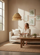 Paniery handwoven natural raffia lampshade with a tiered fringe design, creating a warm, diffused light in a living room setting.
