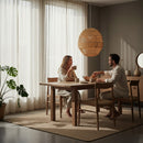 Paniery handwoven natural raffia lampshade, sculptural design, creates ambient light. A couple sits at a dining table below.