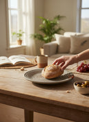 Paniery handwoven grey rope plate with concentric circle design and leather accents, holding a rustic bread roll.