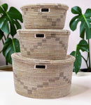 Paniery handwoven Senegalese storage baskets in natural seagrass and recycled plastic with geometric patterns and cut-out handles.