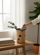 Paniery handwoven natural fiber cylindrical vase with black and tan accents, styled with eucalyptus.