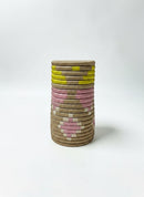 Paniery handwoven natural fiber vase with pink and yellow geometric pattern. Cylindrical decorative piece.