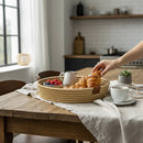 Paniery natural woven tray with croissants, berries, and a pitcher on a rustic wooden table.