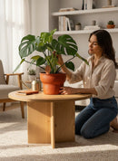 Paniery handwoven drum-inspired basket in orange leather, seagrass, and recycled plastic. A woman tends to a plant in the basket.