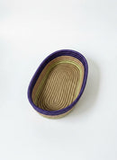 Paniery oval handwoven basket in natural fibers with purple and green accents. Ideal for table or home decor.