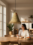 Paniery handwoven natural raffia lampshade with fringed edge, conical shape, hanging above a dining table.