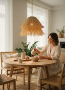 Paniery handwoven natural raffia lampshade with a fringed hem, casting a warm glow over a dining table.