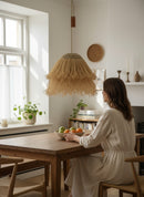 Paniery handwoven natural raffia lampshade with tiered fringe detail, creating a warm, diffused light. Handmade in Morocco.