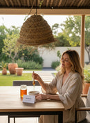 Paniery handwoven natural raffia lampshade with fringed edge hanging outdoors over a woman at a table.
