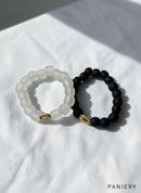 Paniery handmade recycled glass bracelets in matte black and frosted white, each with a gold cowrie shell accent. Unisex design.
