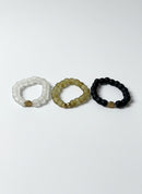 Paniery three recycled glass beaded bracelets in white, tan, and black, each with a unique gold-tone charm.