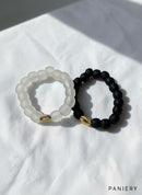 Paniery handcrafted recycled glass bracelets in matte black and frosted white, each with a gold cowrie shell accent.