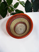 Paniery handwoven Senegal drum-inspired basket in orange leather, seagrass, and recycled plastic with concentric bands of red, yellow, and white.