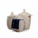 Paniery Senegal handwoven laundry baskets in natural white with leather handles. Three sizes shown, one with a dark blue patterned cloth.