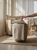 Paniery Senegal handwoven laundry basket made of recycled plastic and natural fibers with leather handles, shown in a neutral-toned room.