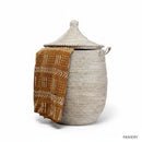 Paniery Senegal handwoven laundry basket in off-white with a brown mud cloth draped over the front. Features leather handles and a lid.