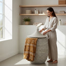 Paniery Senegal handwoven laundry basket in light grey with leather handles, featuring a decorative brown and white patterned throw.