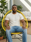 Paniery Signature Solis Chair, a striking yellow radial design chair handwoven from recycled fishing lines, shown with a man sitting outdoors.