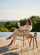 Paniery Signature Solis chair in yellow, handwoven from recycled fishing lines, with black metal legs. Model relaxes outdoors.