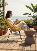 Paniery Signature Solis Chair in yellow, handwoven from recycled fishing lines, with a black metal frame, on a wooden deck by the sea.