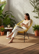 Paniery Signature Solis compact chair in yellow, handwoven from recycled fishing lines, with a woman relaxing on a patio.