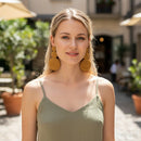 Paniery mustard yellow handwoven spiral statement earrings on a blonde model wearing a green camisole.