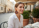 Paniery orange and navy blue handwoven spiral statement earrings worn by a smiling woman outdoors.