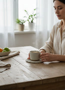 Paniery handwoven white coaster with grey stripes, protecting a mug of coffee on a wooden table.