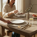 Paniery handwoven white placemat with a textured weave, protecting a wooden table. A white plate sits on the placemat.