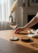 Paniery handcrafted wooden coasters with a natural wood grain and a unique black and white patterned inlay. A wine glass rests on one coaster.
