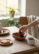 Paniery handcrafted wooden heart bowl filled with berries, with a slice of bread and coffee on a wooden table.