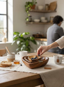 Paniery handcrafted wooden heart bowls with natural African design, stacked and filled with blueberries. A hand is adding blueberries to the top bowl.