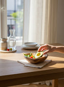 Paniery handcrafted wooden heart bowl with African design, filled with salad and avocado, on a table.