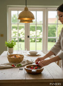 Paniery handcrafted natural wood serving bowl with handles, filled with fresh berries. A woman adds more berries to the bowl.