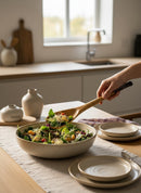 Paniery handcrafted wooden spoon serving a fresh salad from a speckled ceramic bowl in a bright kitchen.