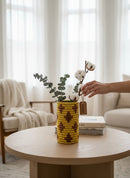Paniery yellow and brown handwoven vase with diamond pattern, styled with eucalyptus and cotton branches on a coffee table.